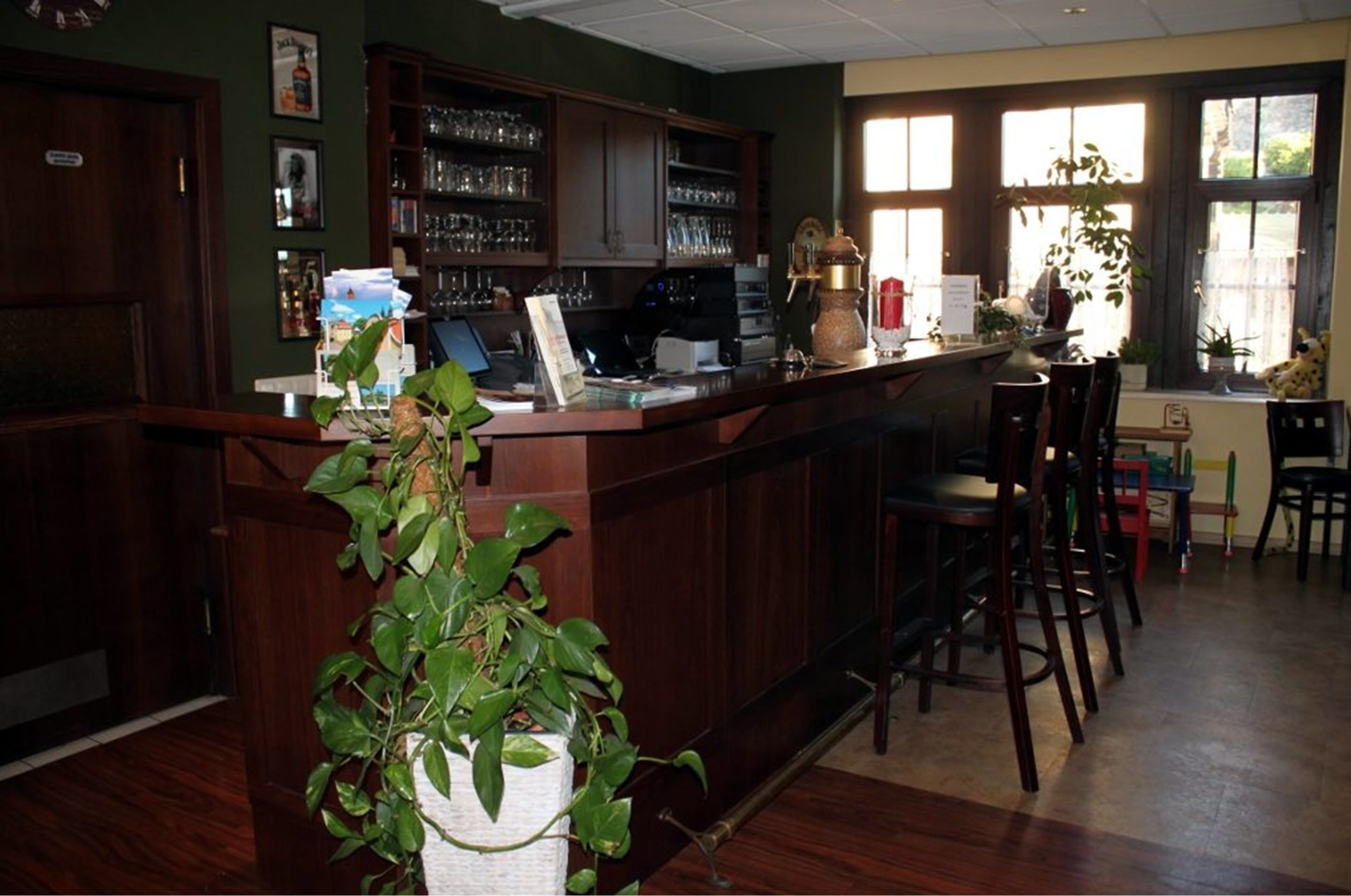 Zona de bar con muebles de madera, una barra con una computadora y estantes con vasos.