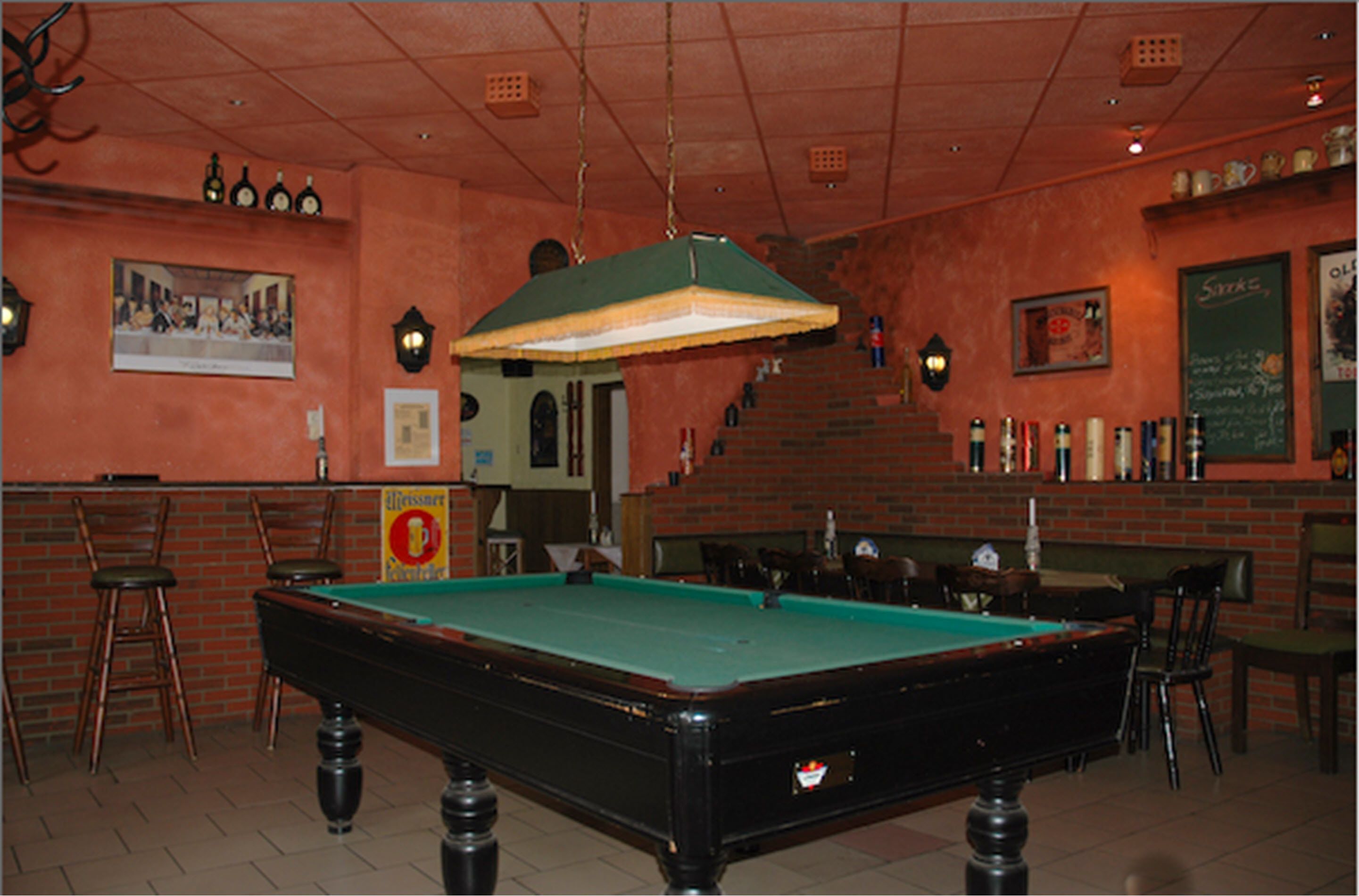 Un tavolo da biliardo in una stanza con pareti in mattoni, un'area bar e una scala.