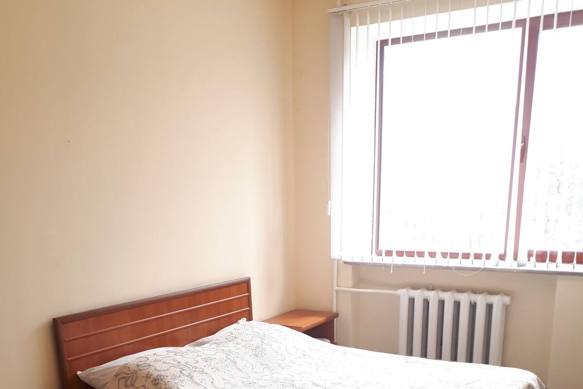 A bedroom with a wooden bed, a nightstand, a radiator, and a window with blinds.
