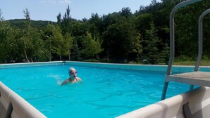 Una piscina con agua cristalina azul, rodeada de árboles y una escalera de metal.