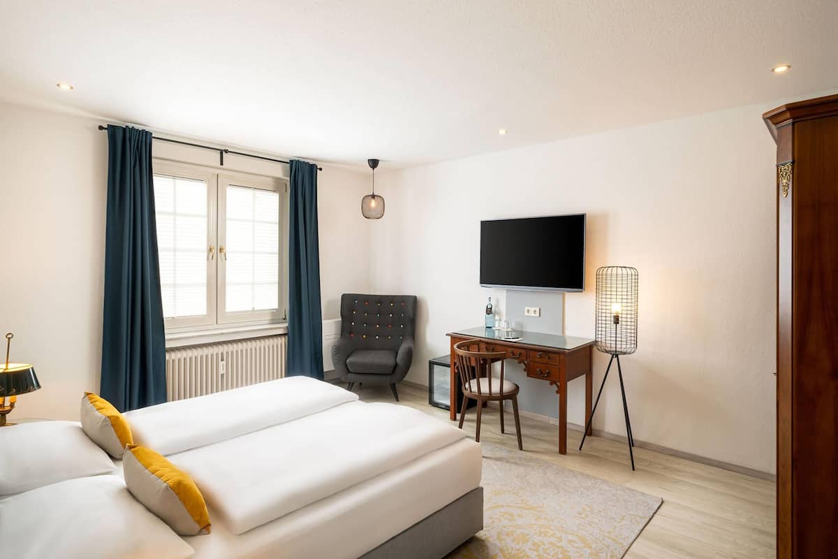 A hotel room with a bed, desk, chair, TV, and a radiator.