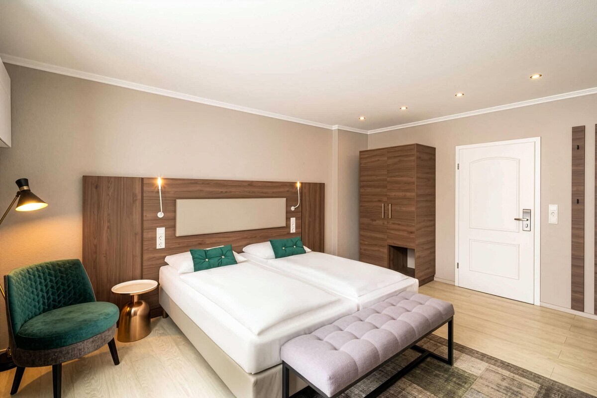 A modern bedroom with a large bed, bedside tables, a green armchair, and a bench.
