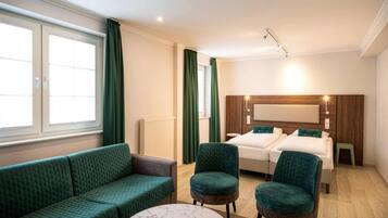 A hotel room with a bed, a sofa, two armchairs, a round table, and a large window with curtains.