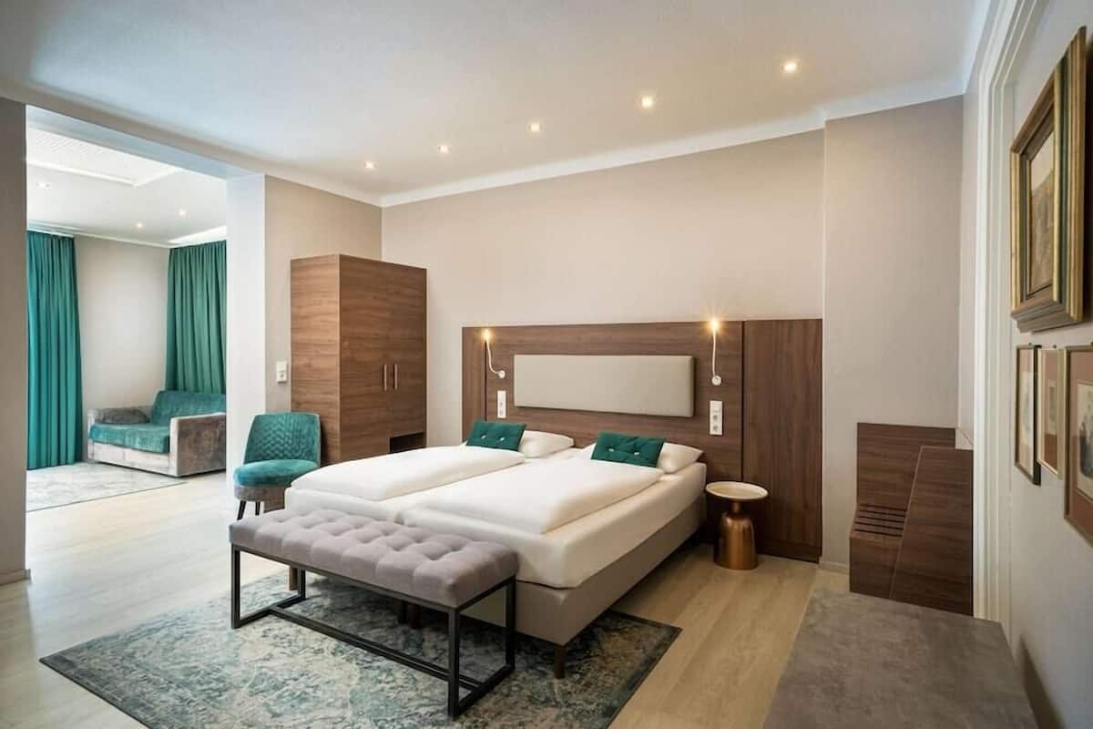 A modern bedroom with two beds, a bench, a bedside table, and a view of a living area.
