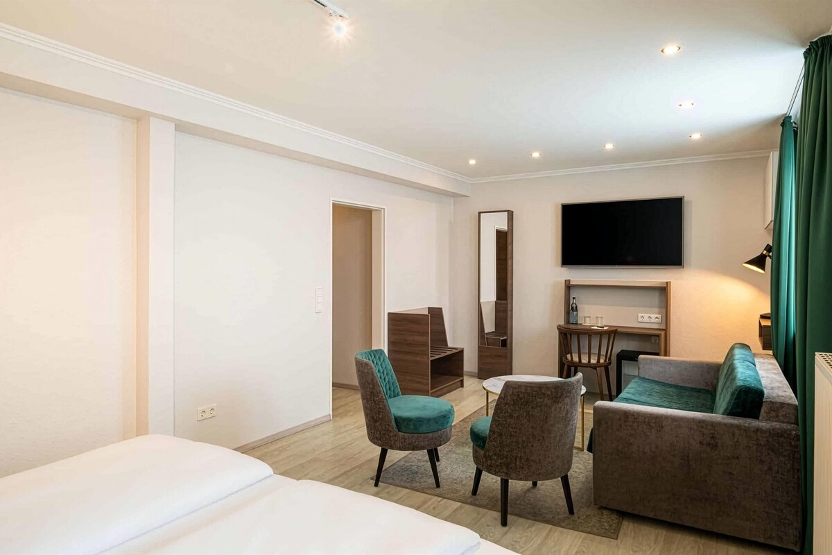 A hotel room with a bed, two armchairs, a sofa, a TV, and a desk with a mirror.