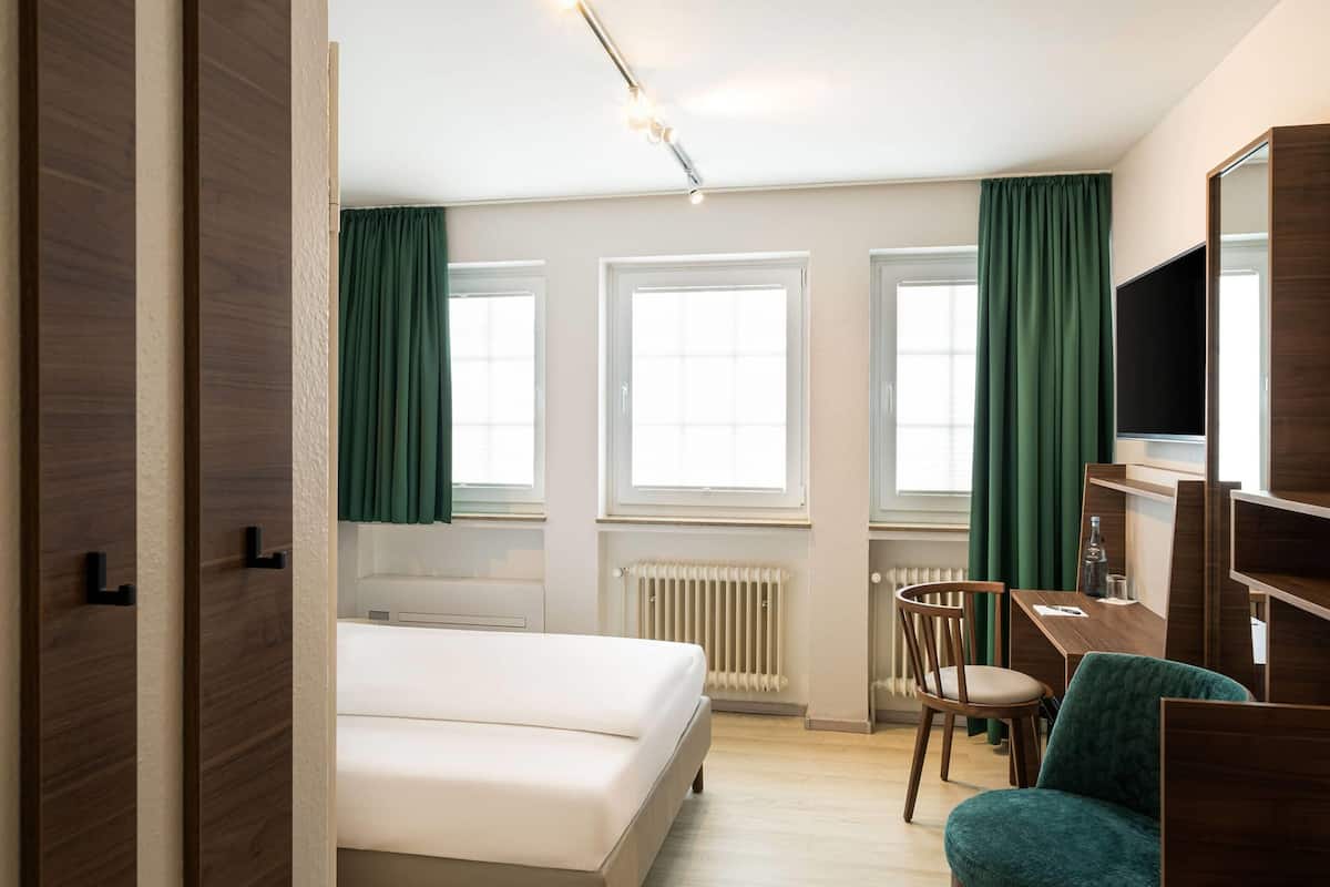 A bedroom with a bed, a desk, a chair, and a TV.