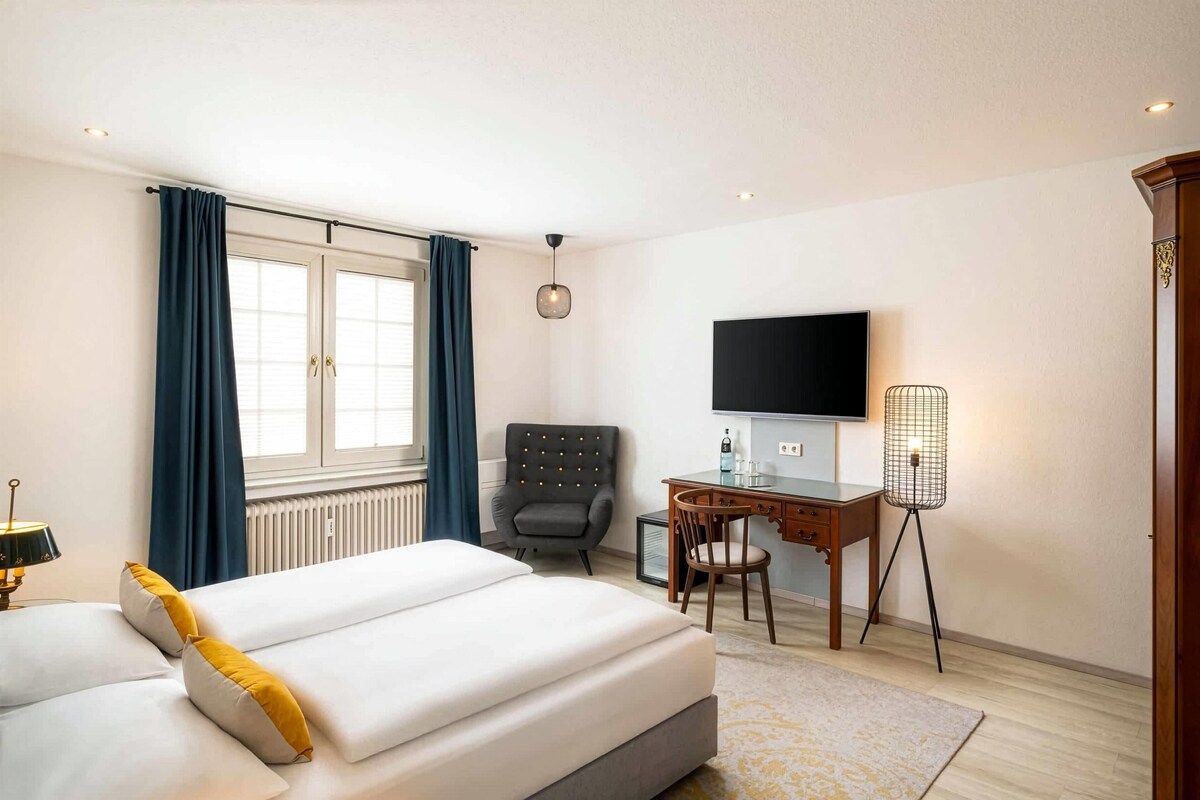 A hotel room with a bed, a desk, a chair, a television, and a radiator.