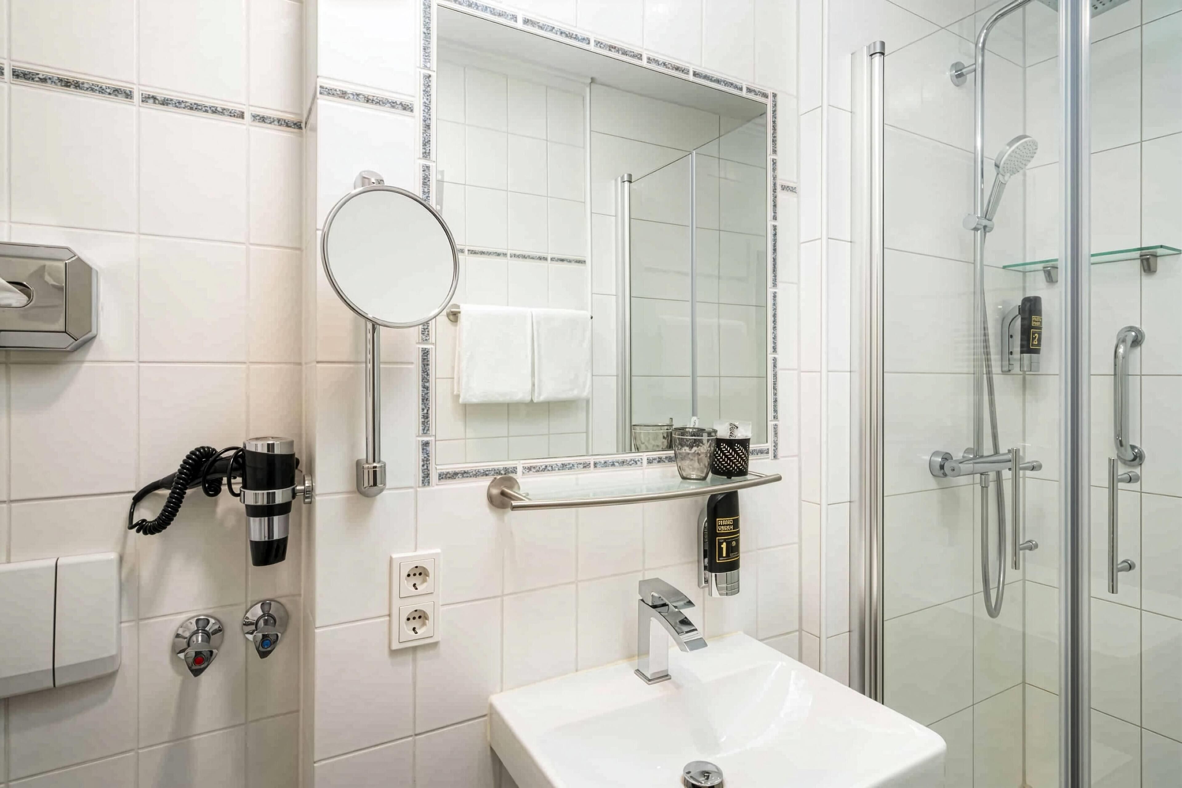 Un baño moderno con un lavamanos blanco, un espejo redondo, un cabezal de ducha de mano y un perchero.