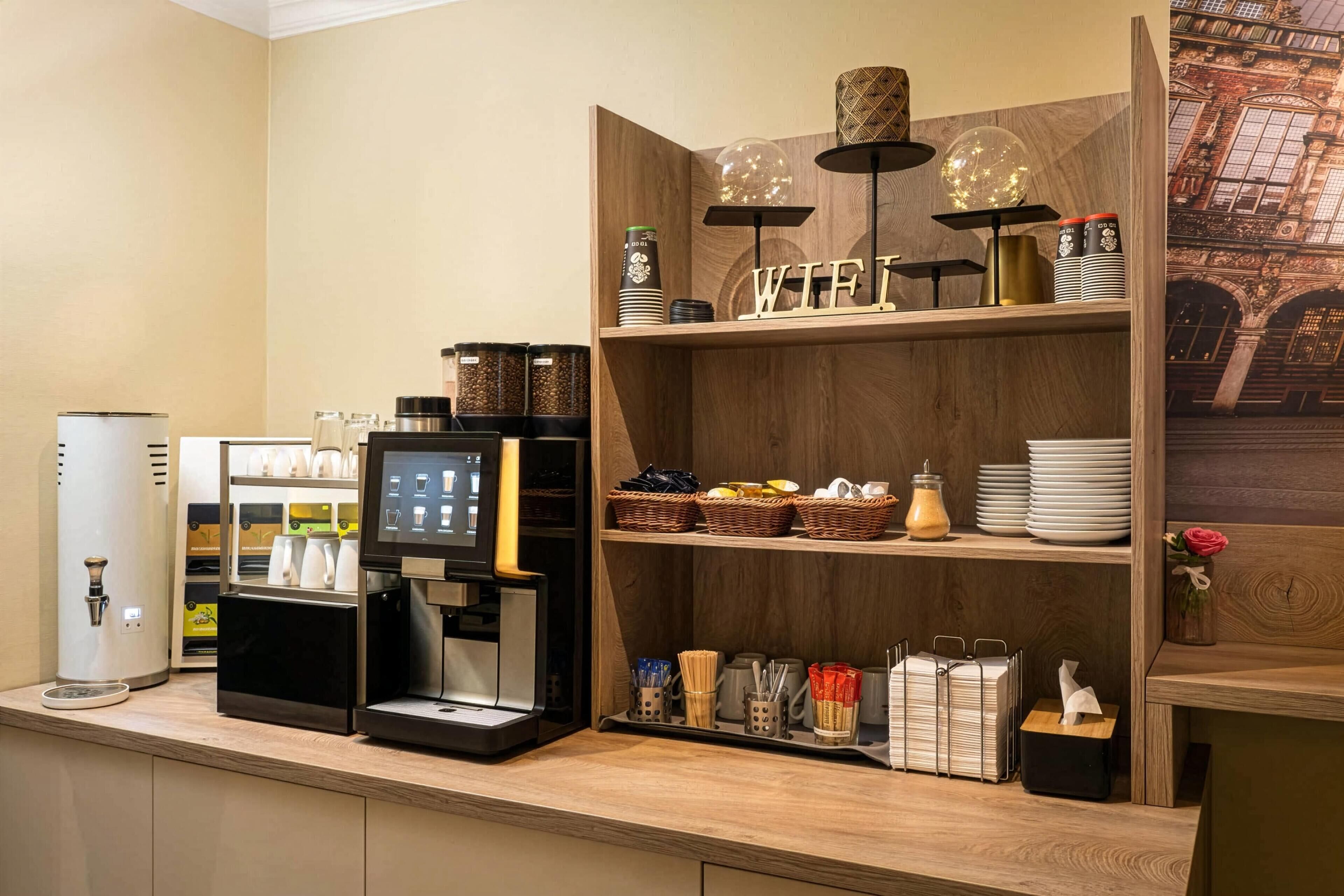 A coffee station with a coffee machine, a tea dispenser, and a selection of mugs and cups.