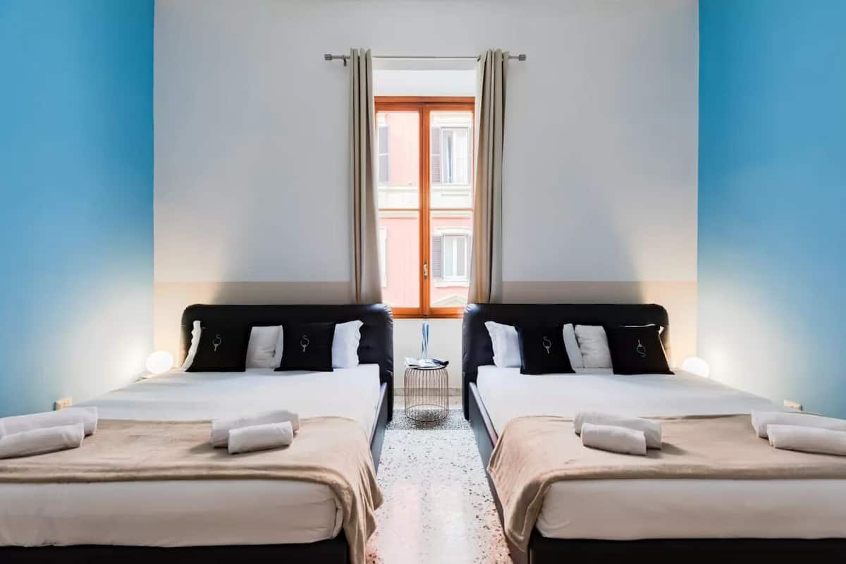A hotel room with two beds, a small table, and a window with curtains.