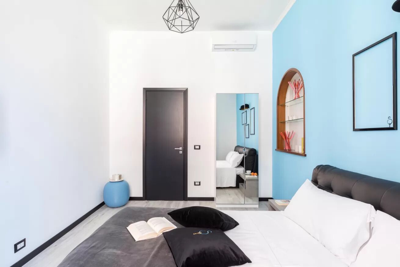 Ein modernes Schlafzimmer mit Bett, Leseecke, Kleiderschrank und angrenzendem Badezimmer, durch eine Glastür sichtbar.