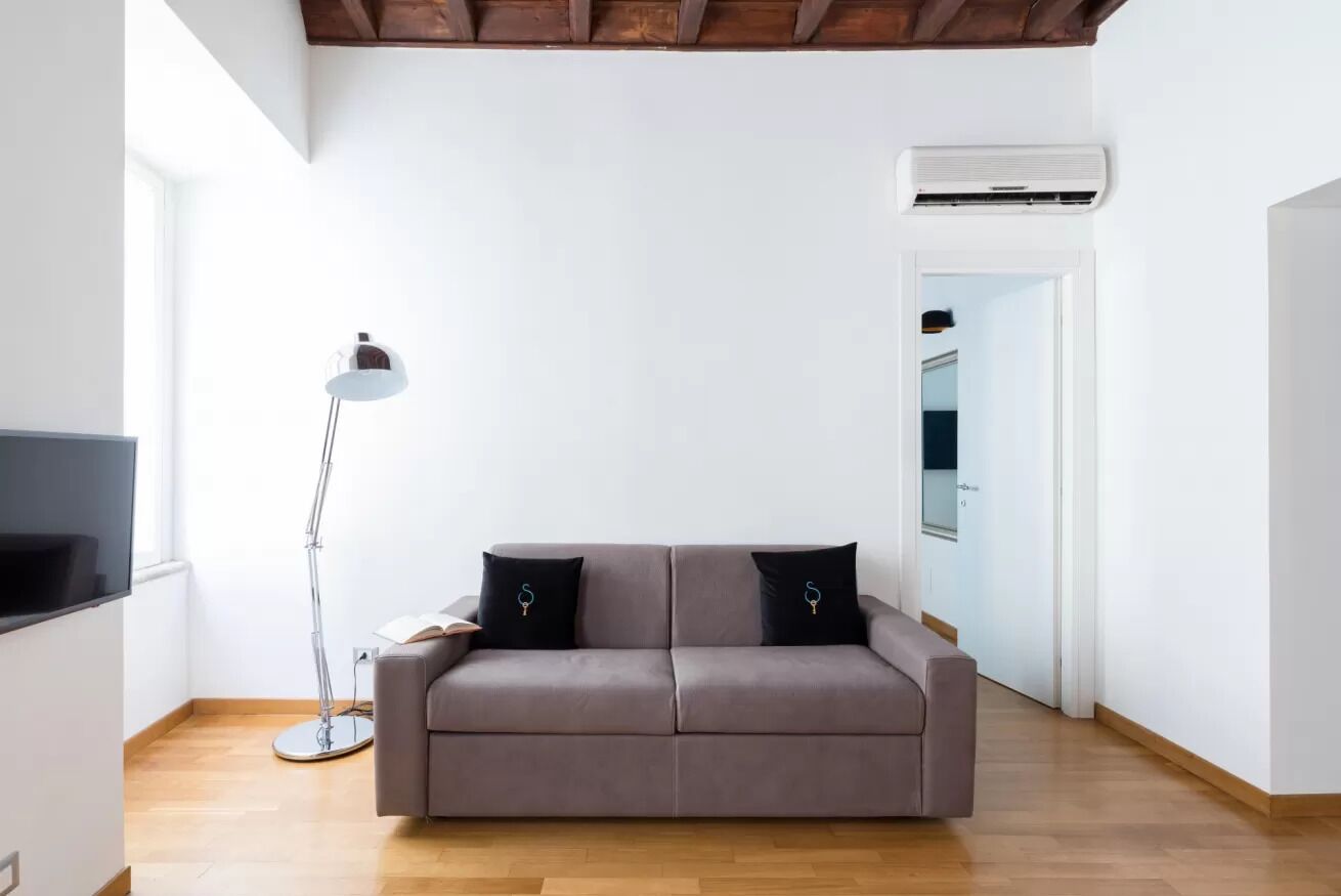 A modern living room with a grey sofa, a floor lamp, and an air conditioning unit on the wall.