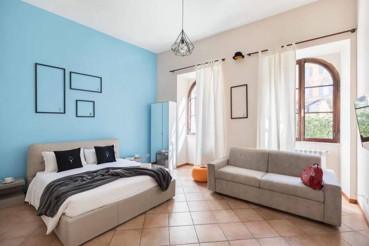 A bedroom with a bed, a sofa, and a window with curtains.