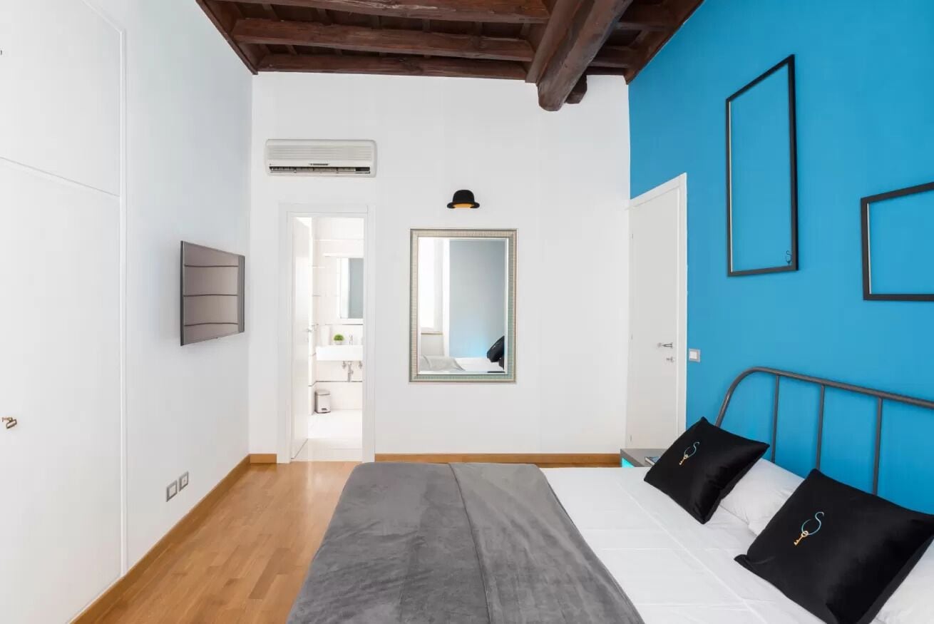 Een slaapkamer met een bed, een spiegel en een televisie aan de muur.