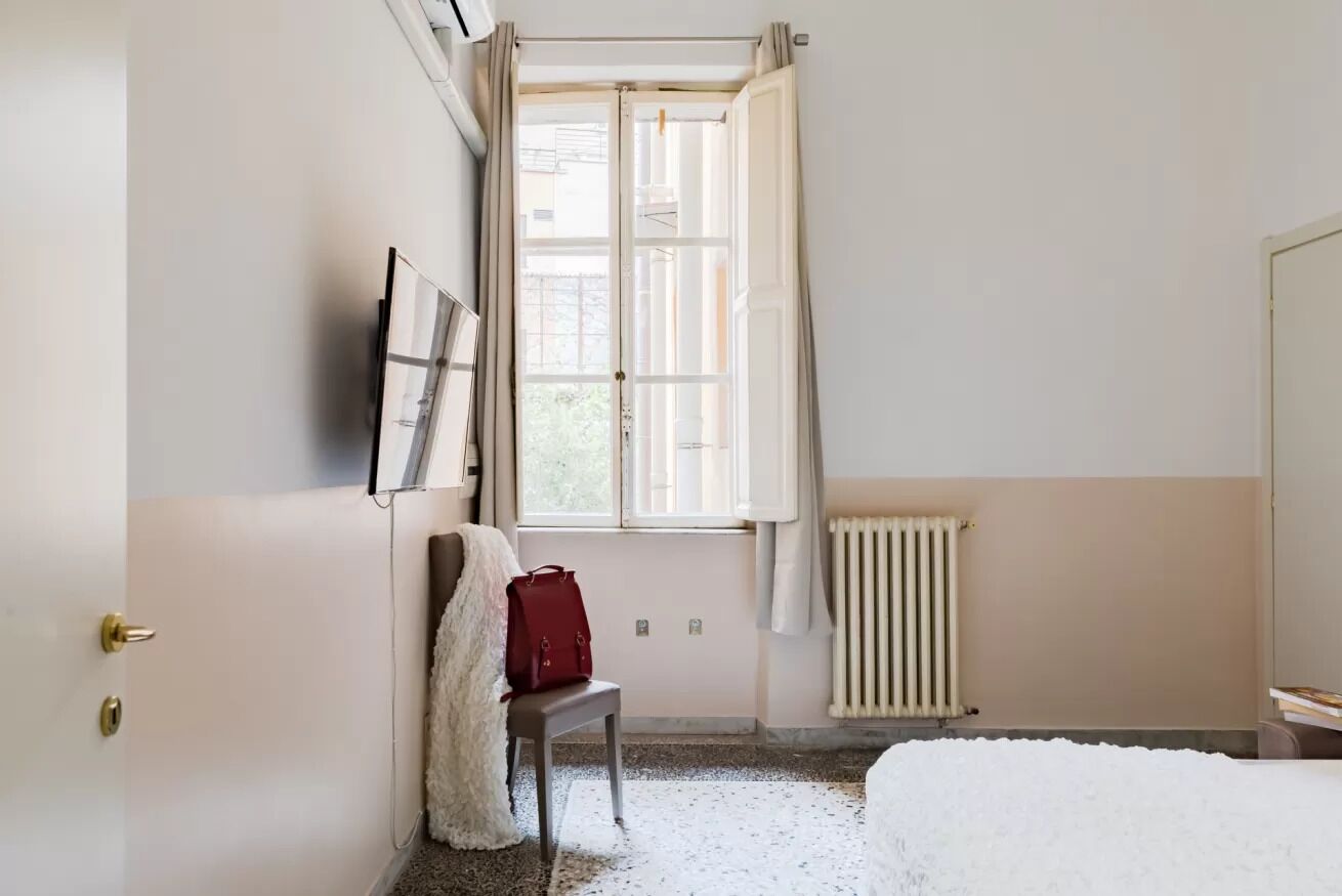 A bedroom with a bed, a chair, a radiator, and a window with curtains.