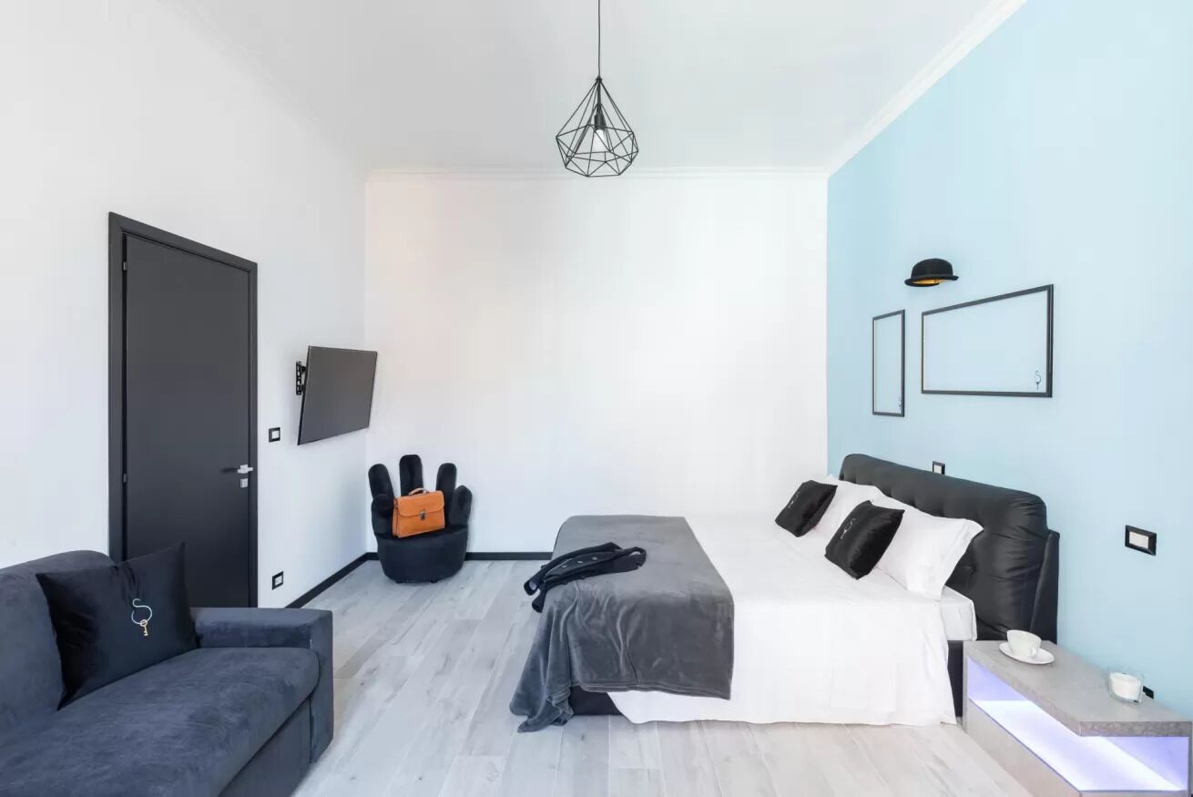 A modern bedroom with a bed, a sofa, a desk, and a hanging light fixture.
