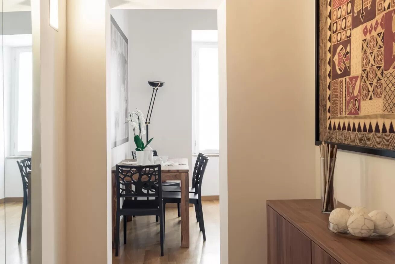 Zona pranzo con tavolo e sedie in legno, una lampada da terra e un elemento decorativo a parete.