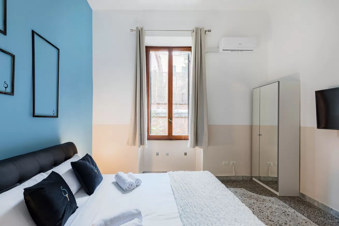 Una habitación de hotel con cama, armario, ventana con cortinas y aire acondicionado.