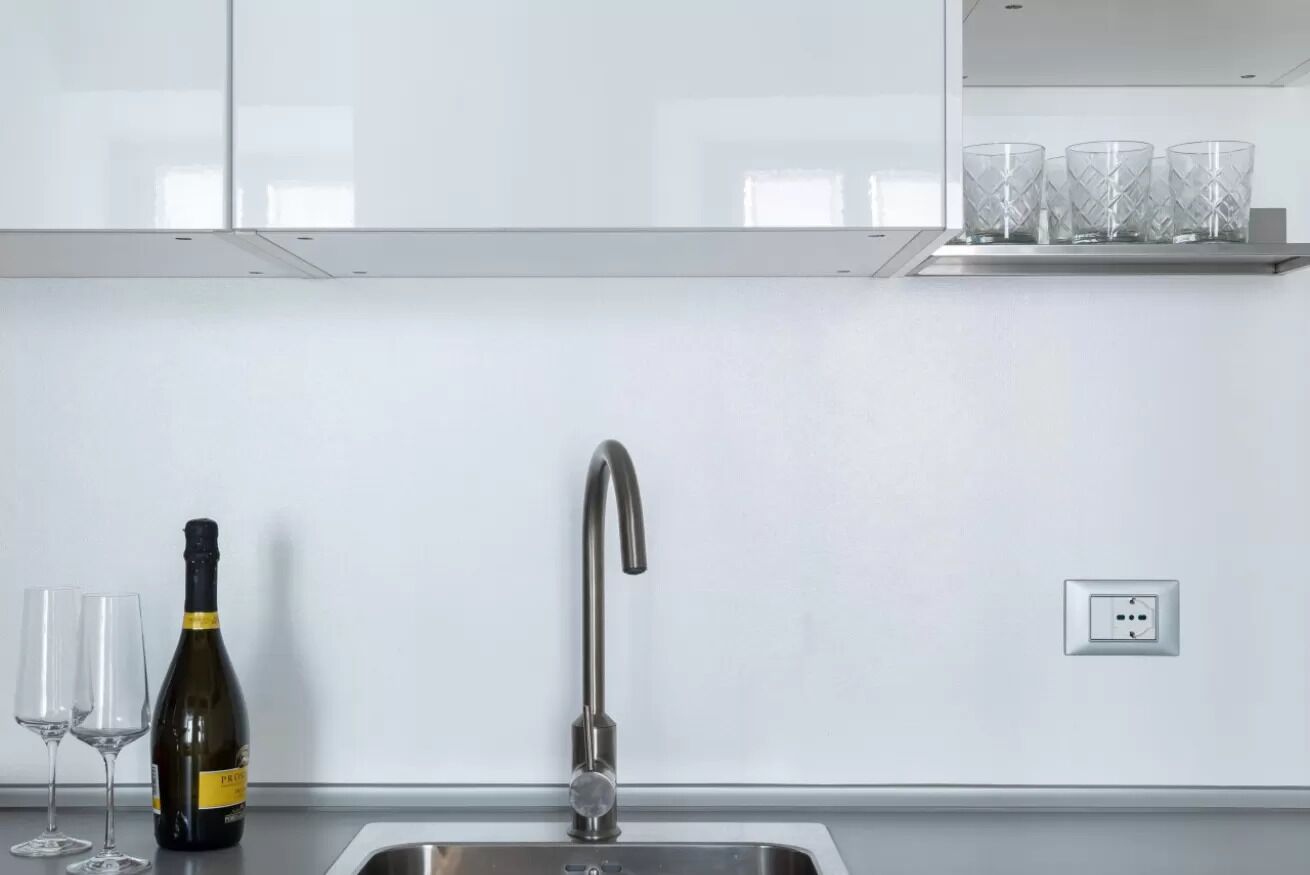 A modern kitchen with a stainless steel sink, a wine bottle, and two glasses.