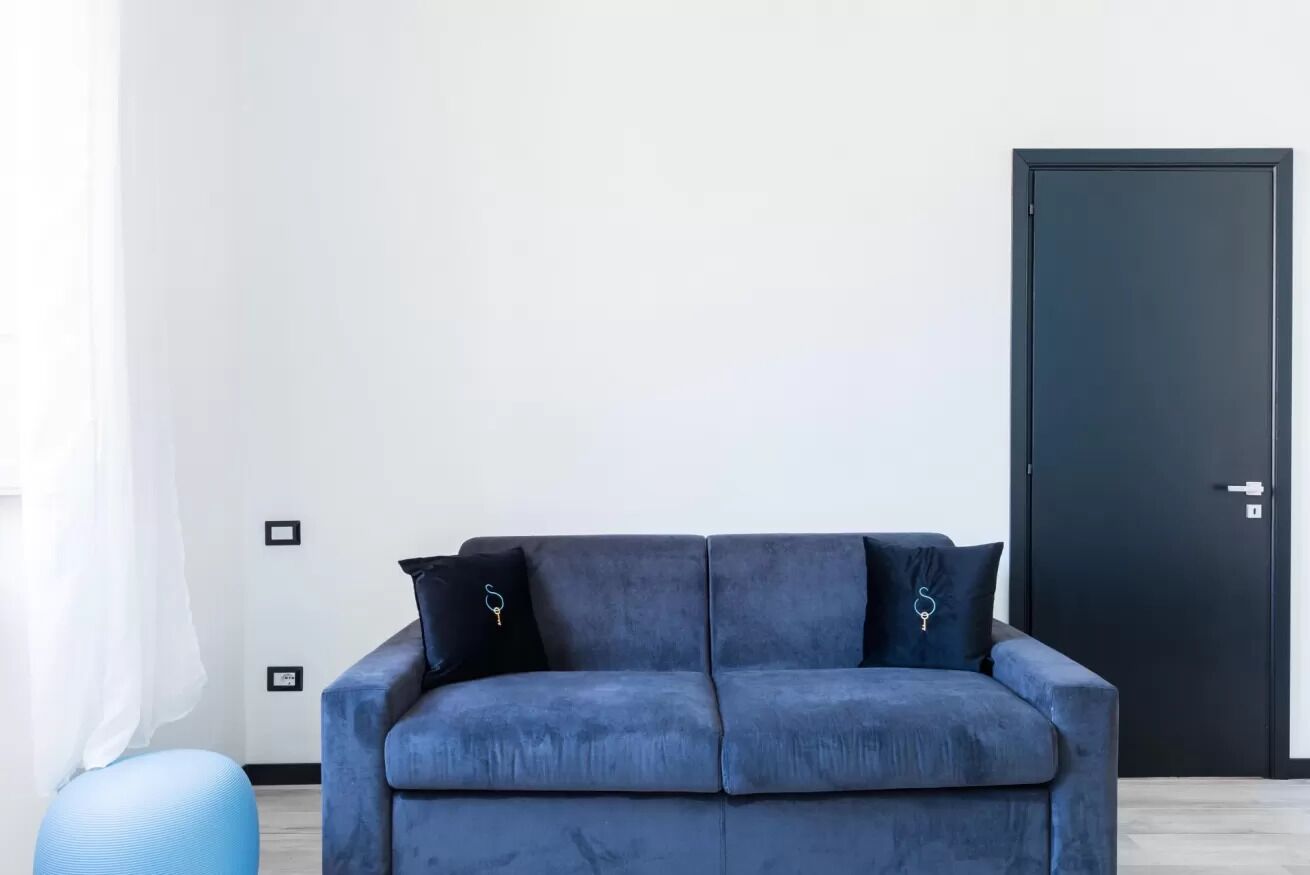 Un salon moderne avec un canapé bleu foncé, deux coussins assortis, un pouf bleu clair et une porte sombre.