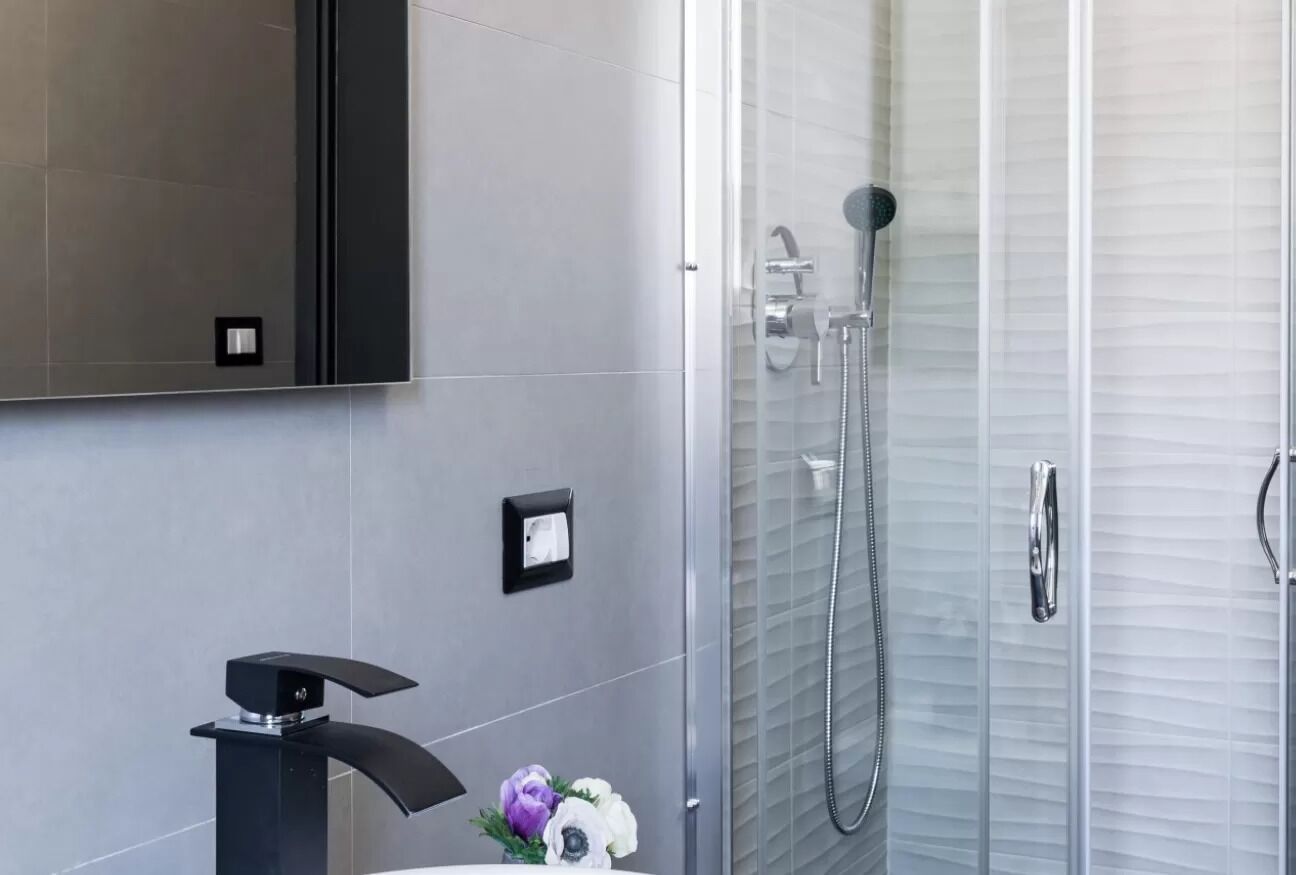 A modern bathroom with a glass-enclosed shower, a black faucet, and a wall-mounted mirror.