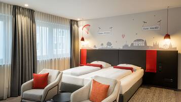 A hotel room with two beds, a sofa, and a chair. There are curtains, a wall mural, and a ceiling light.