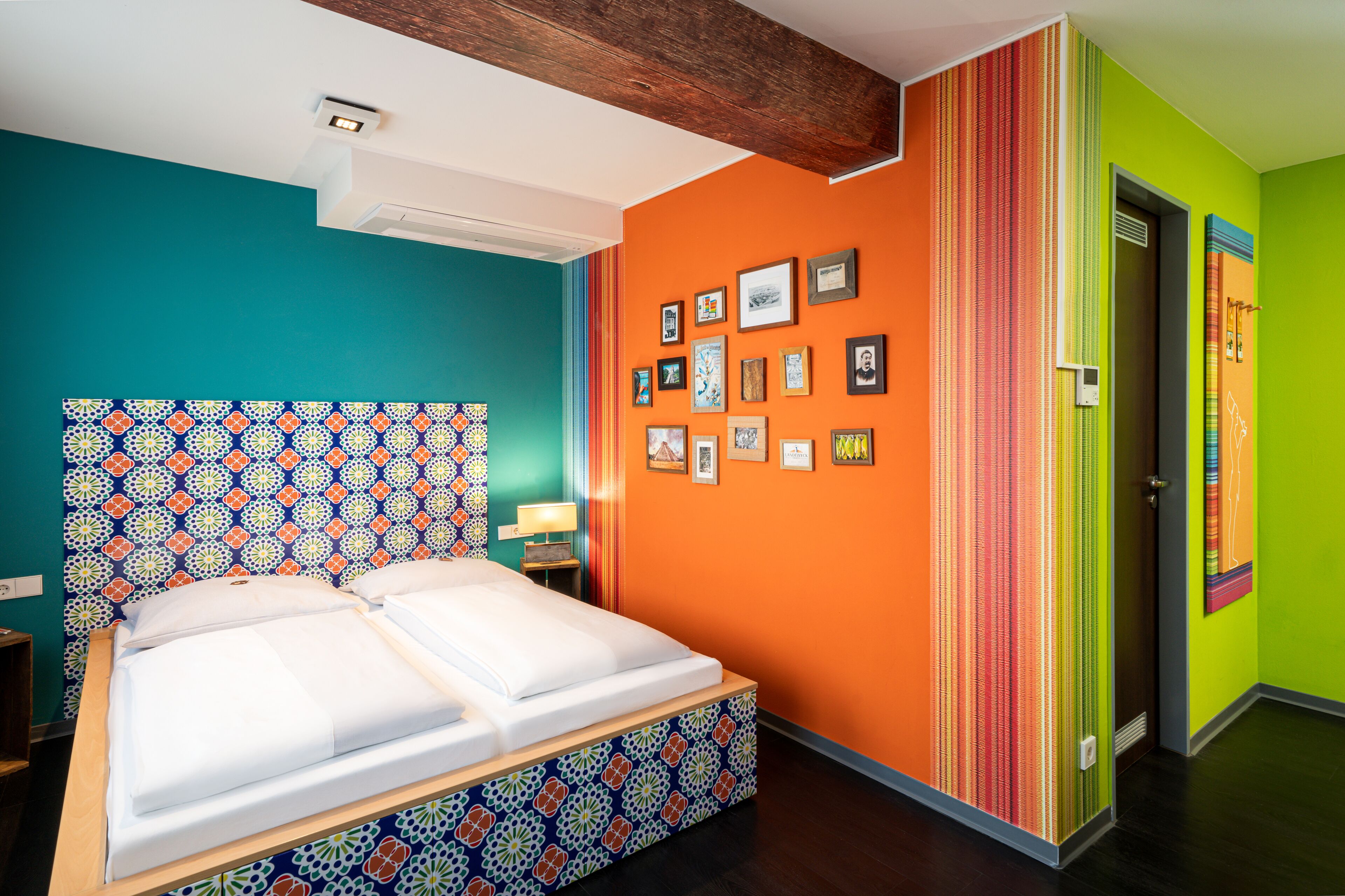 Een kamer met een bed, een hoofdeinde met een patroon, een muur met ingekaderde foto's en een deur met strepen.