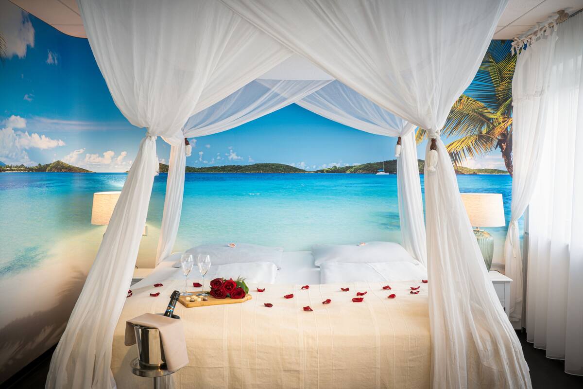 A four-poster canopy bed with a view of a tropical beach and ocean.