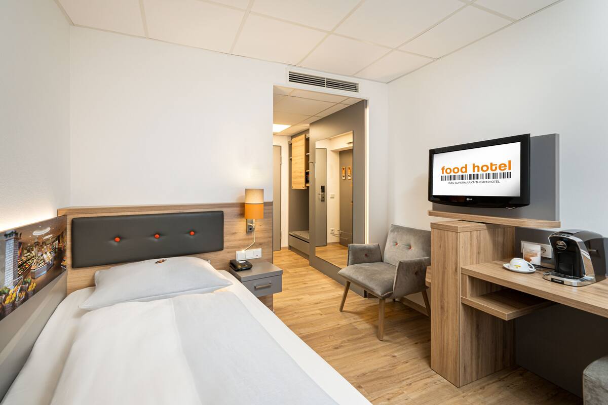 A hotel room with a bed, a desk with a computer, a chair, a television, and a coffee maker.