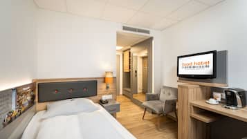 Habitación de hotel con cama, escritorio con computadora, silla, televisor y cafetera.