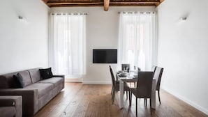 A modern living room with a wooden ceiling, a sofa, a dining table with chairs, and a flat-screen TV mounted on the wall.