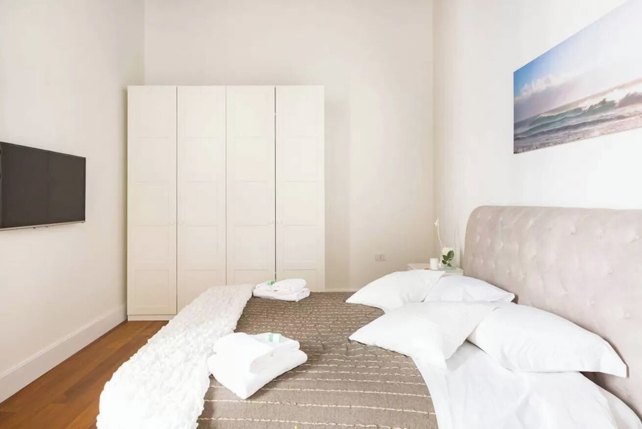Een slaapkamer met een bed, een kledingkast, een flatscreen televisie en een schilderij aan de muur.