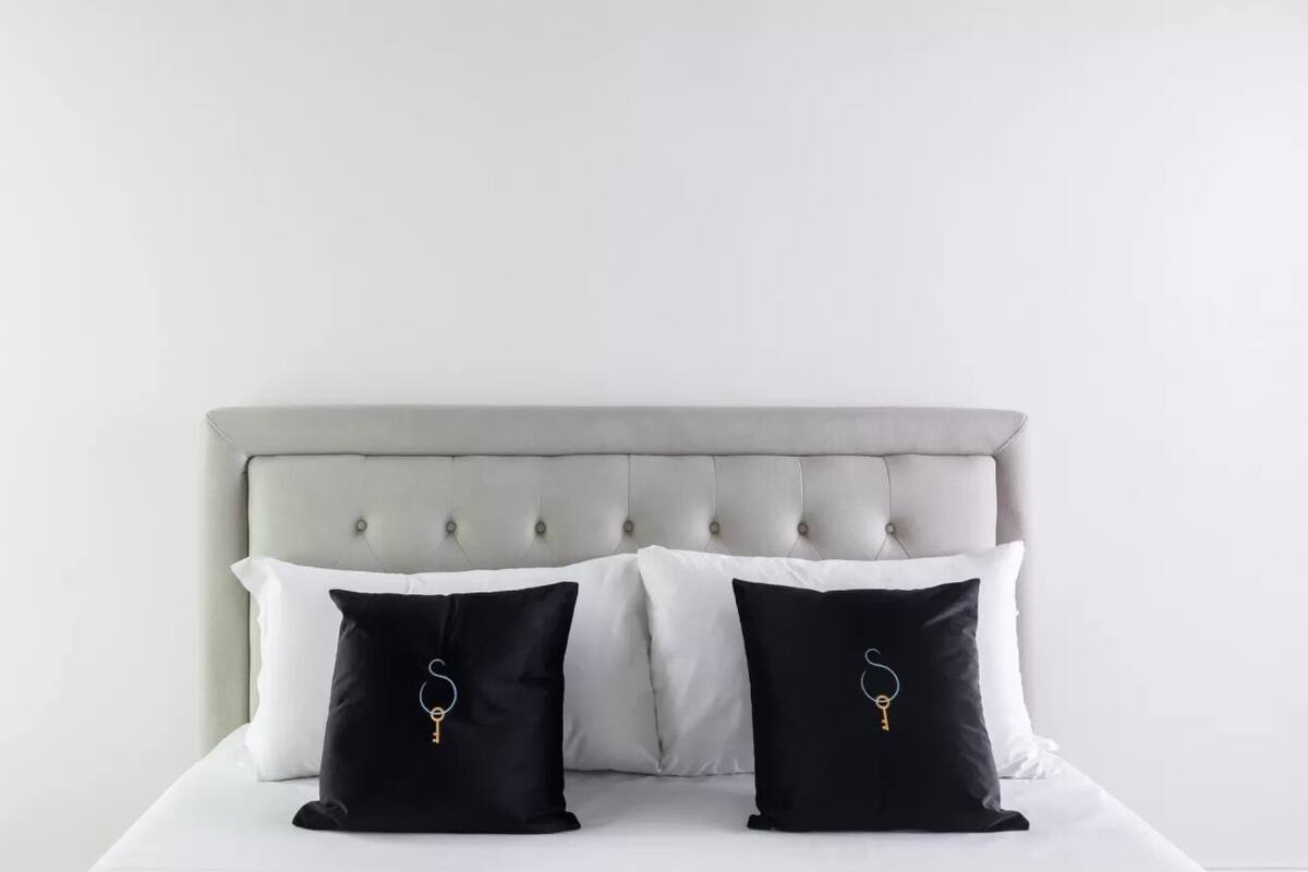 A bed with a tufted headboard and two pillows, one black and one white, with a key design.