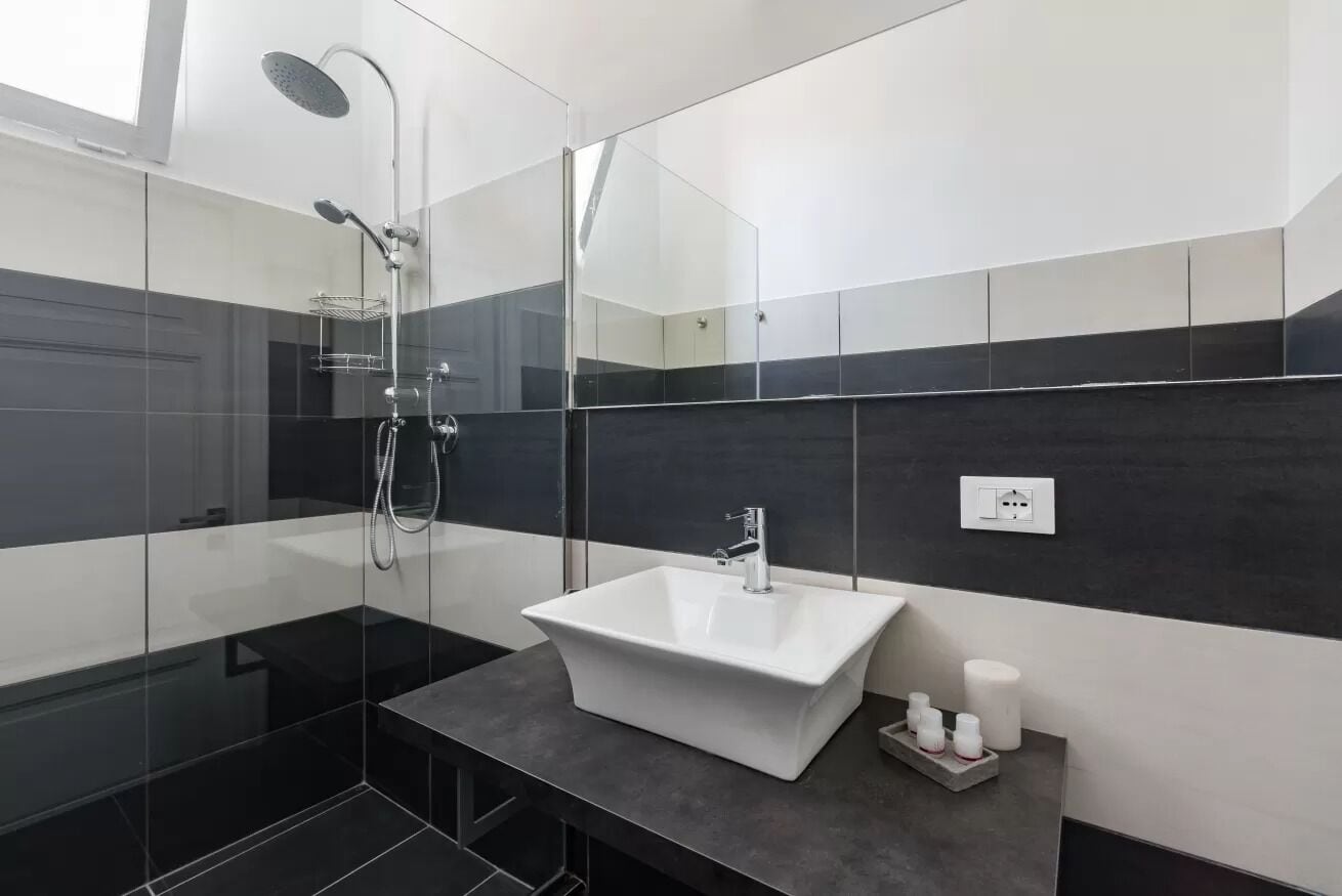 A modern bathroom with a glass-enclosed shower, a white sink, and a mirror.