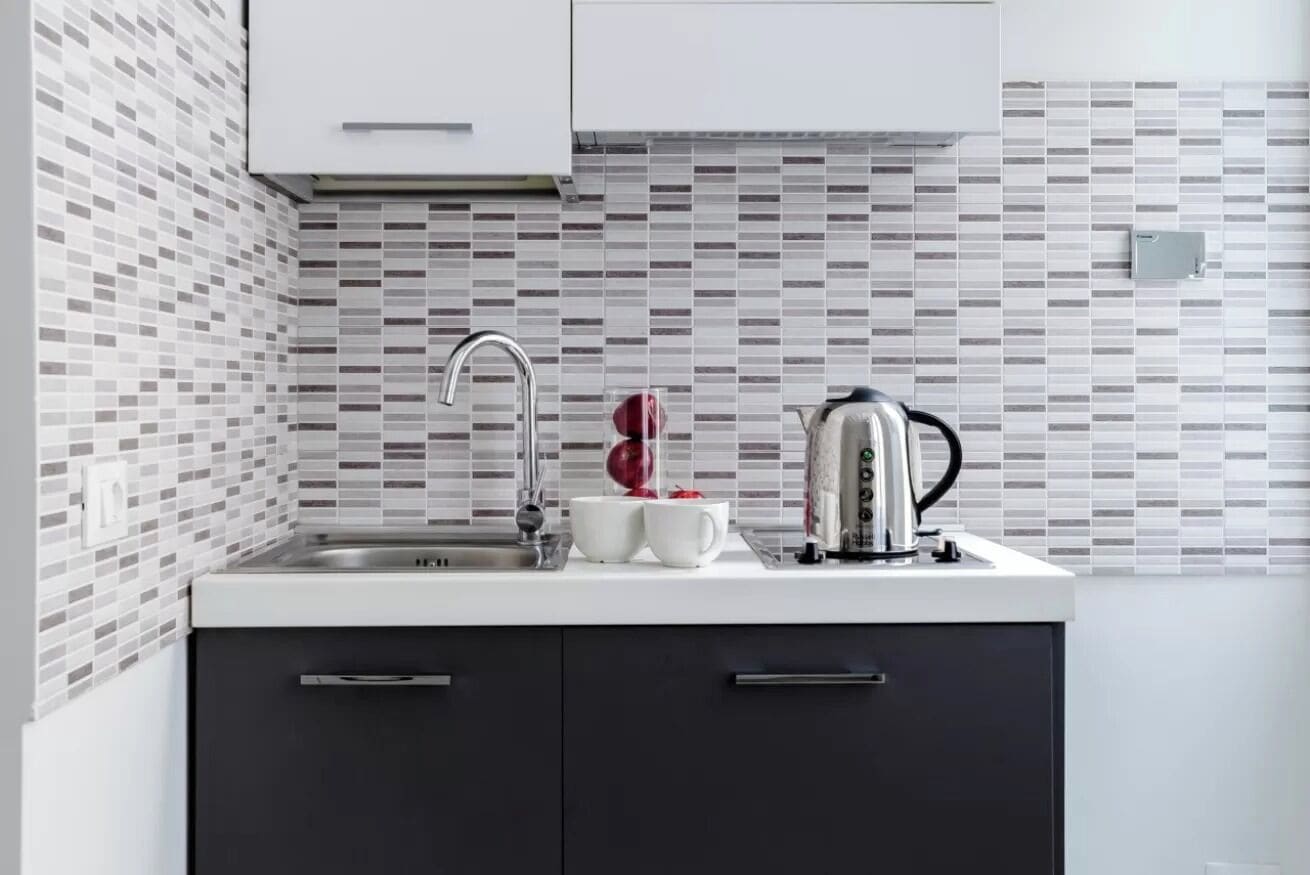 Una cucina moderna con un piano di lavoro bianco, un bollitore in acciaio inossidabile e due tazze bianche.