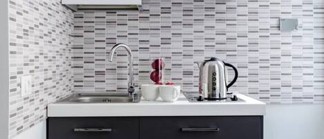 Una cucina moderna con un piano di lavoro bianco, un bollitore in acciaio inossidabile e due tazze bianche.