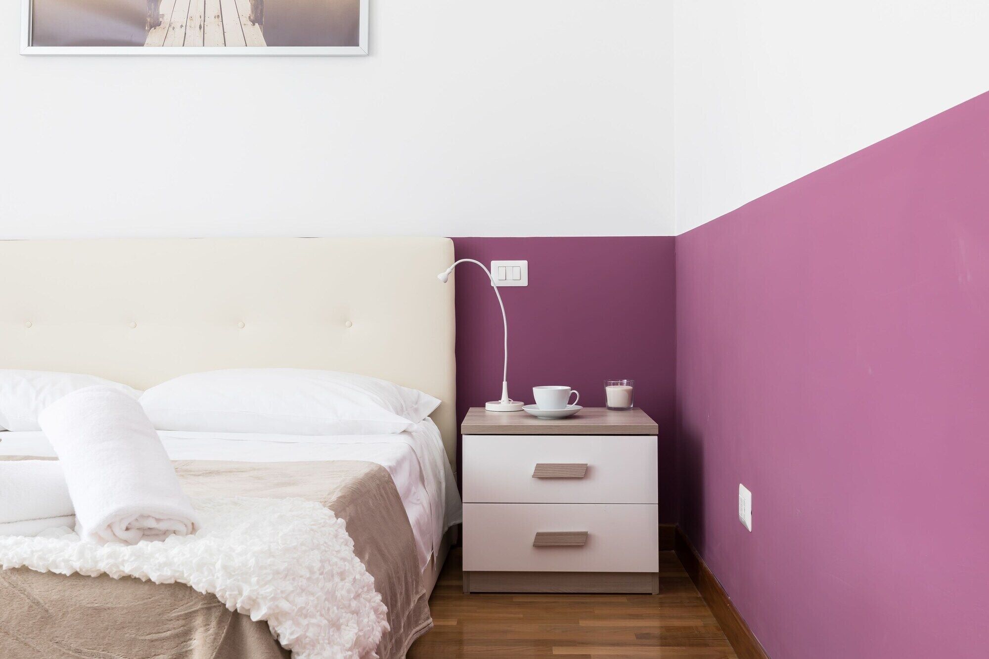 Un dormitorio con una cama, una mesita de noche con una lámpara, una taza y un vaso de leche.