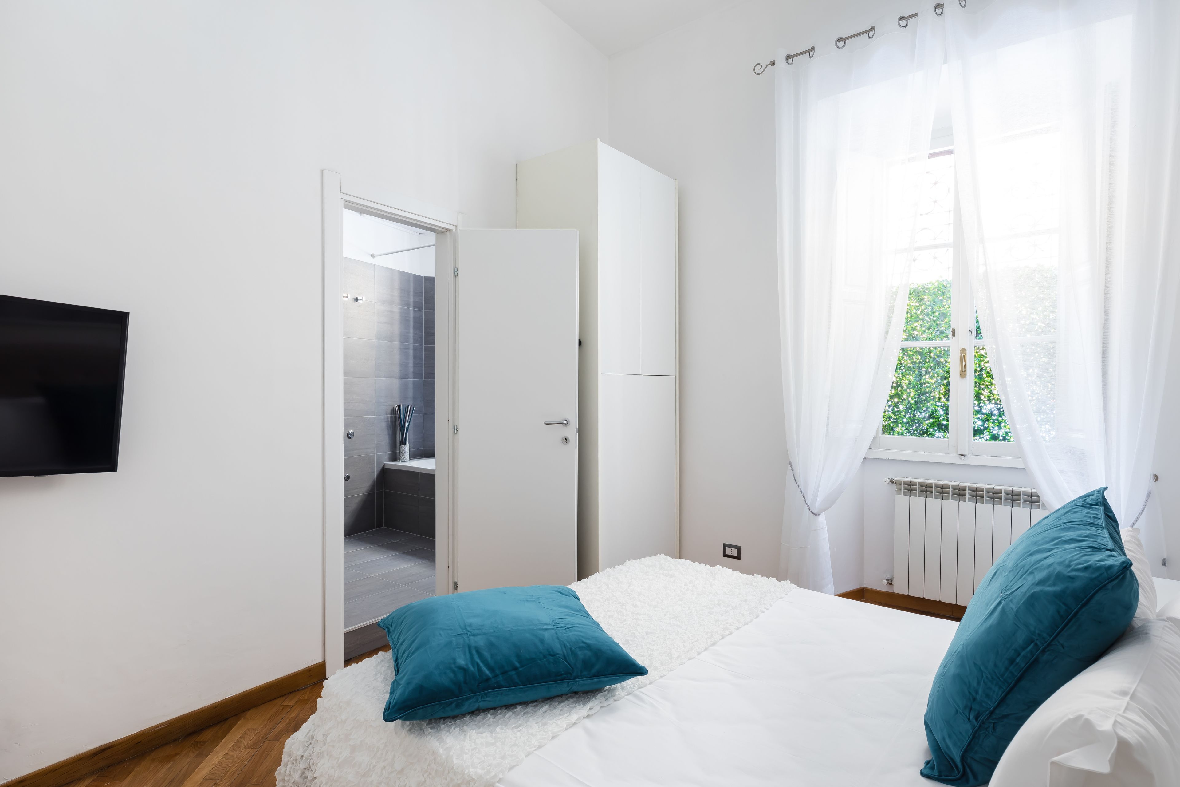 Une chambre à coucher comprenant un lit, une télévision, une armoire et une salle de bain visible à travers une porte ouverte.