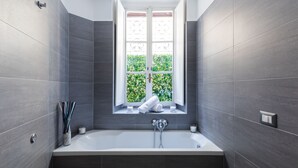 A modern bathroom with a bathtub, a window with a view of greenery, and a towel rack. - A World Aparts - 32 Calabria (Rome)
