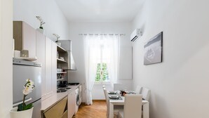A compact kitchen with white cabinets, a built-in oven, and a dining area with a table and chairs. - A World Aparts - 32 Calabria (Rome)
