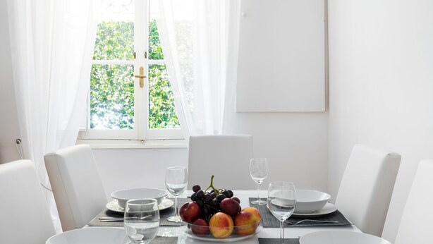 A dining table set with white plates, bowls, and glasses, and a fruit bowl with grapes and peaches. - A World Aparts - 32 Calabria (Rome)