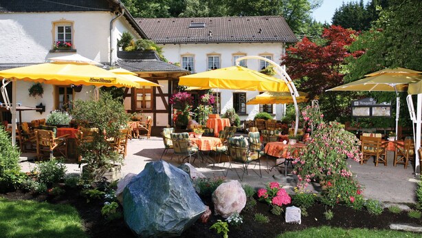 An outdoor café with yellow umbrellas, wooden furniture, and a garden setting. - Rengser Mühle (Bergneustadt)