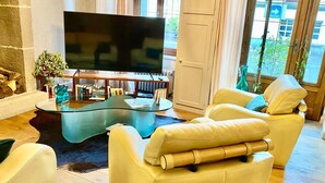 Ein modernes Wohnzimmer mit einem Glastisch, Ledersesseln, einem Flachbildfernseher und einem Bücherregal.