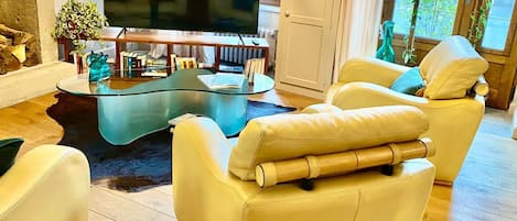 Una sala de estar moderna con una mesa de centro de vidrio, sillones de cuero, un televisor de pantalla plana y una estantería.