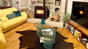 Ein gemütliches Wohnzimmer mit Kamin aus Stein, einem gelben Sofa, einem Glastisch und einem Bücherregal.