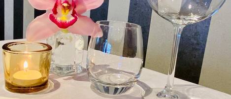 A table with a candle, a glass, and a clear bottle, with a striped wall in the background.