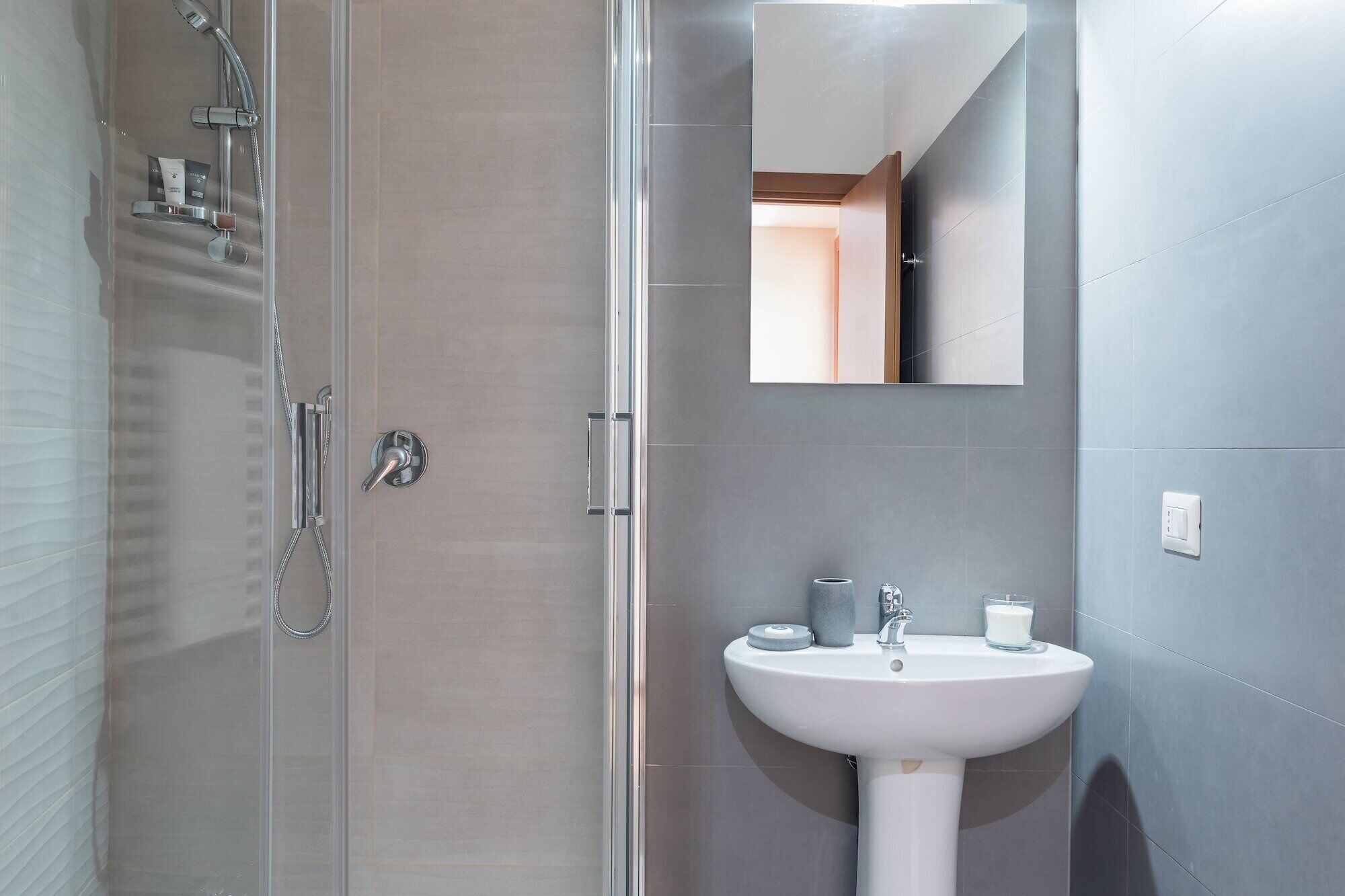 A modern bathroom with a glass-enclosed shower, a white pedestal sink, and a mirror above the sink.