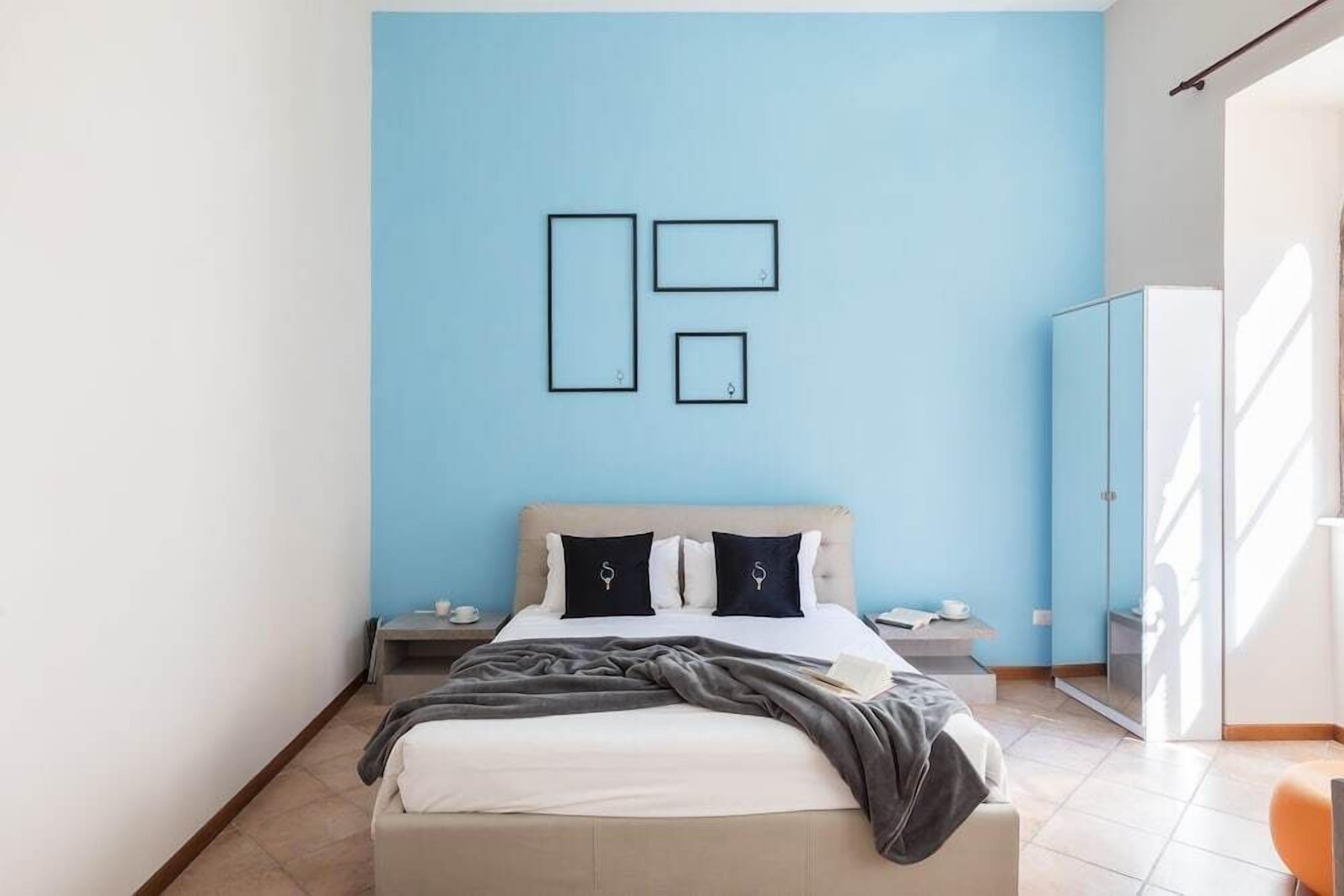 A modern bedroom with a bed, bedside tables, a wardrobe, and a blue accent wall.