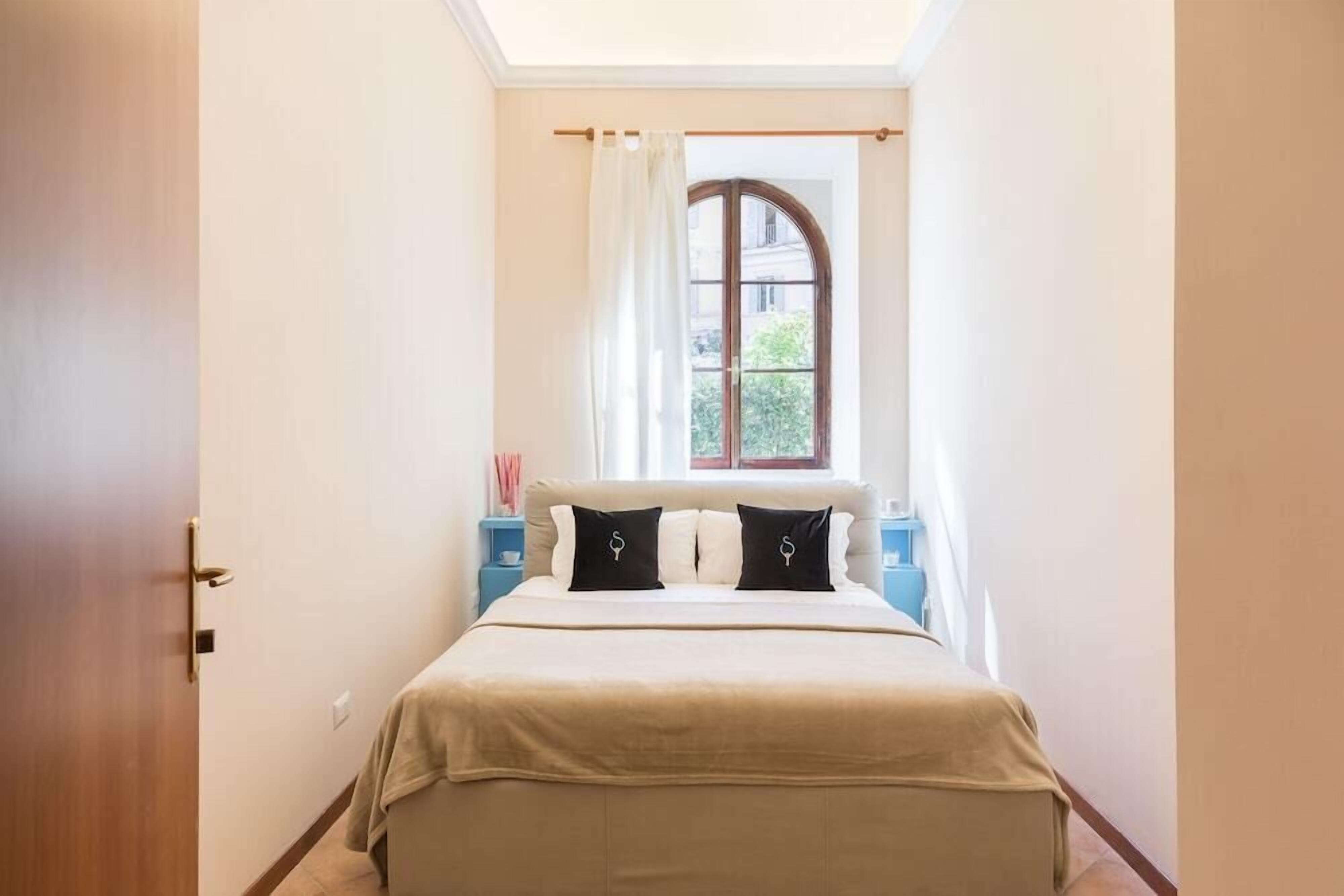 Une chambre à coucher avec un lit, une fenêtre avec des rideaux, une table de chevet et une porte.