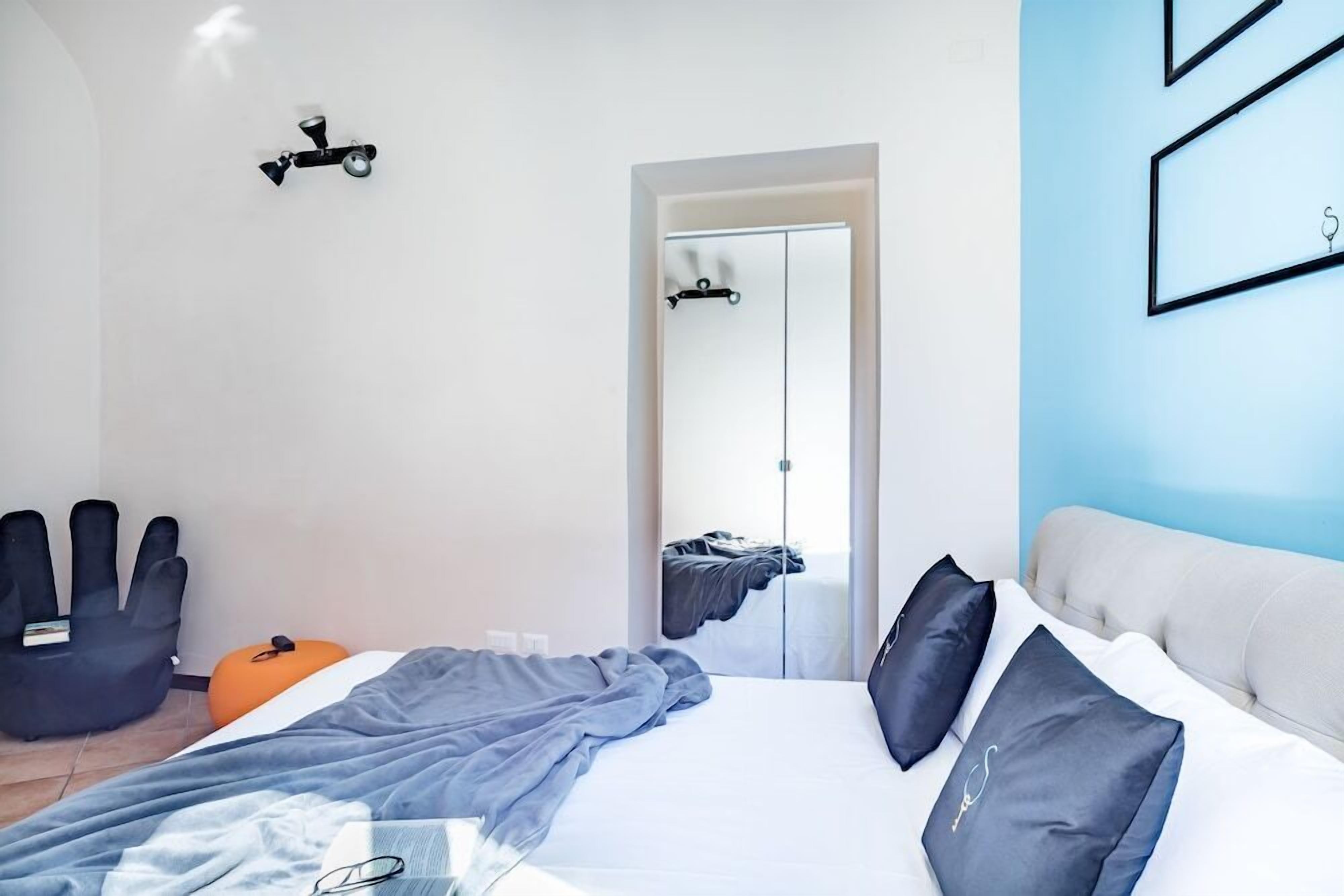 Ein modernes Schlafzimmer mit einem Bett, einem Sessel, einem kleinen orangefarbenen Hocker und einem Spiegel.